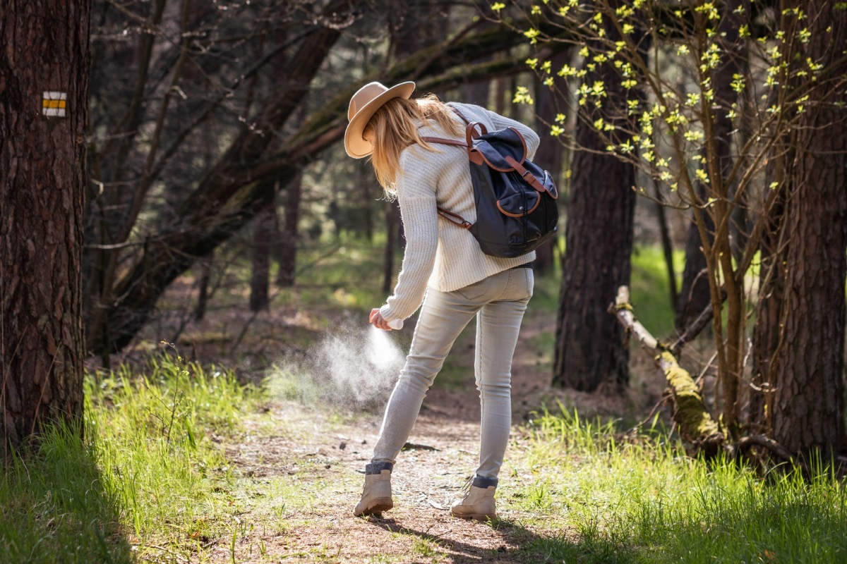 woman outdoors spraying bug spray on clothing