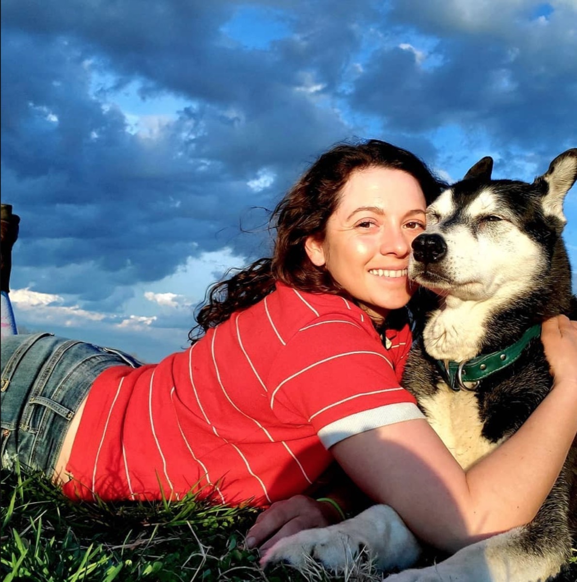 Mackenzie Rosman lying down in a red shirt hugging a black and white dog outdoors
