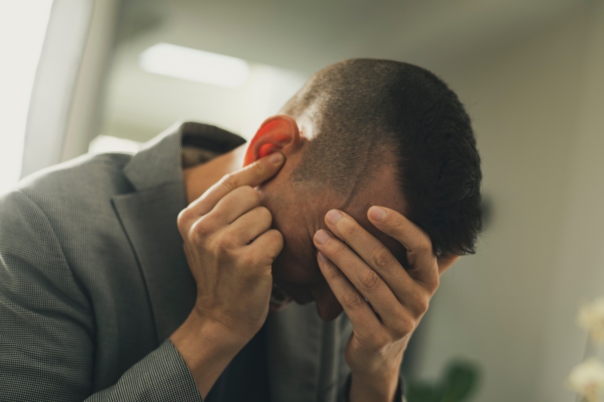 closeup of a suffering man with one hand in his head and the other hand covering his ear