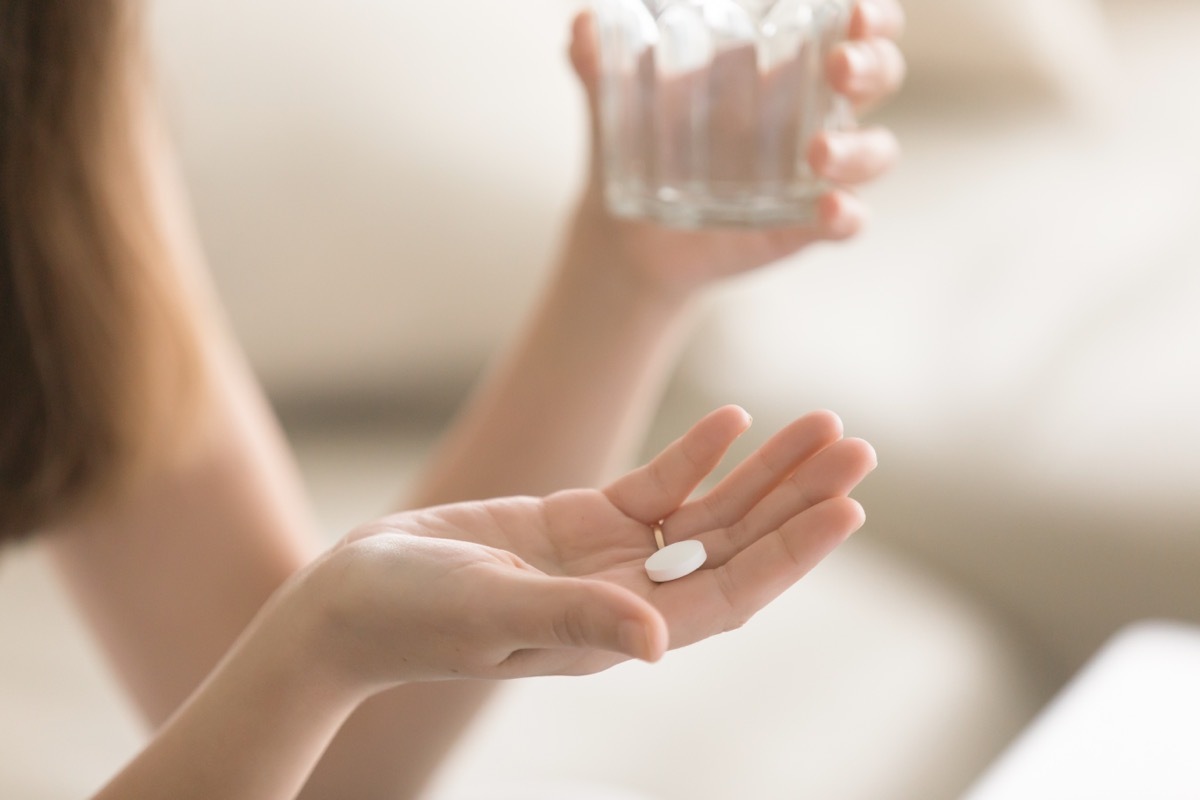 woman with pill in hand holding glass of water