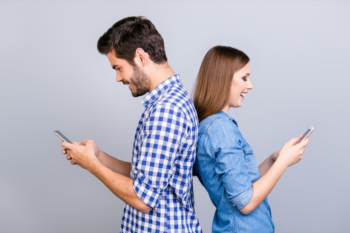 Man and woman standing back to back texting