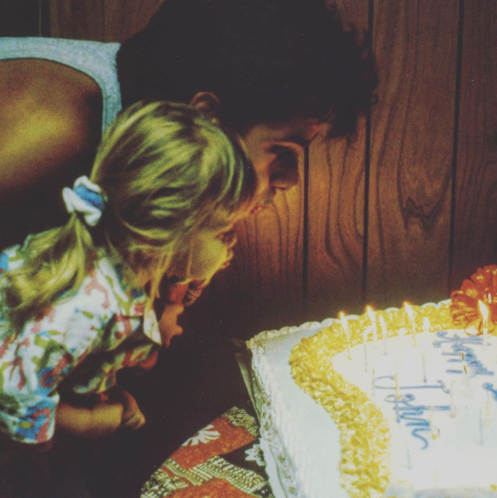 John Stamos blowing out candles on a birthday cake while holding one of the Olsen twins