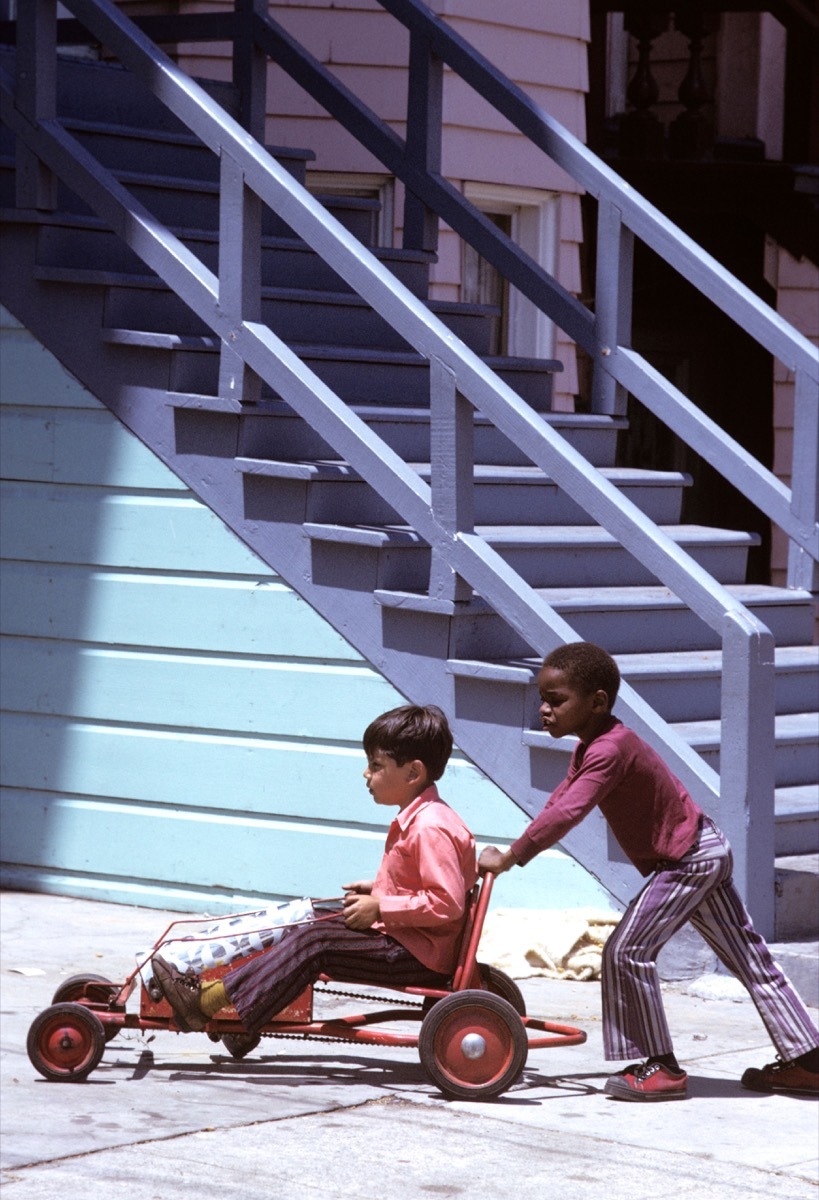 A black boy and Hispanic boy play with homemade go cart wagon in the inner city mission district of San Francisco in 1960s/70s