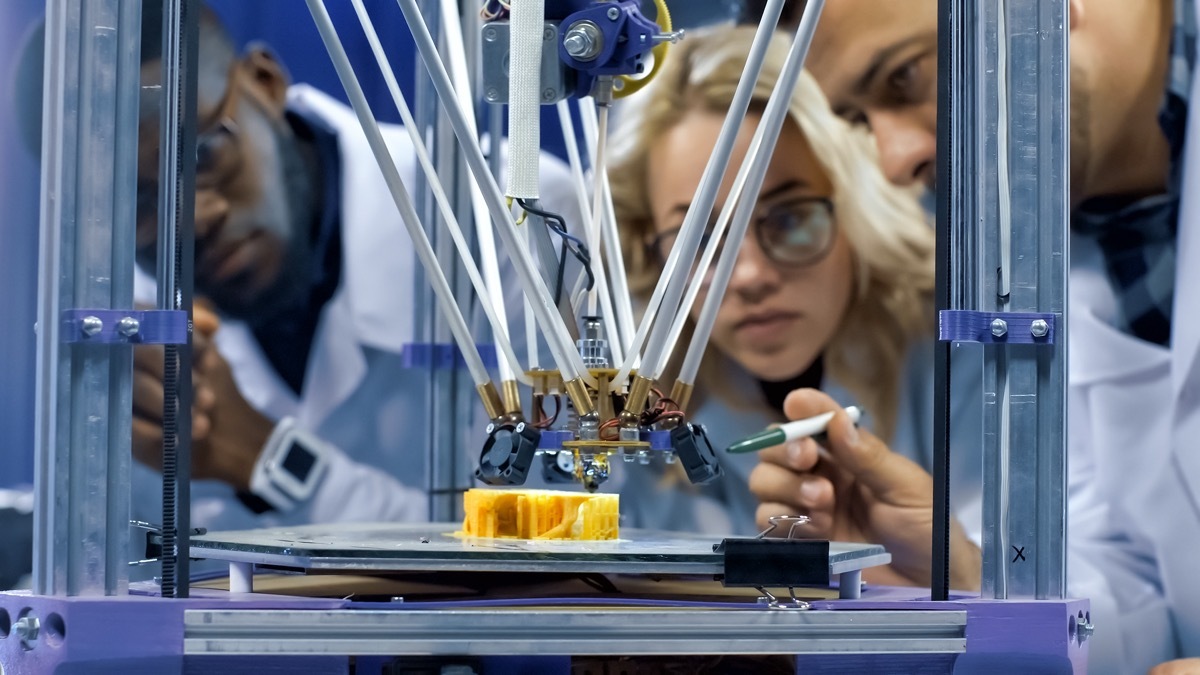 scientists gathering around 3-D printer and watching process of model production in laboratory