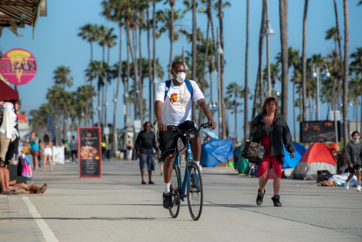 Man wears face mask to protect from coronavirus infection while riding bike on famous Venice Beach boardwalk