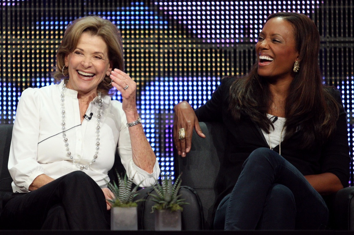 jessica walter in a white top and black pants laughing with aisha tyler in a black and white outfit, both seated