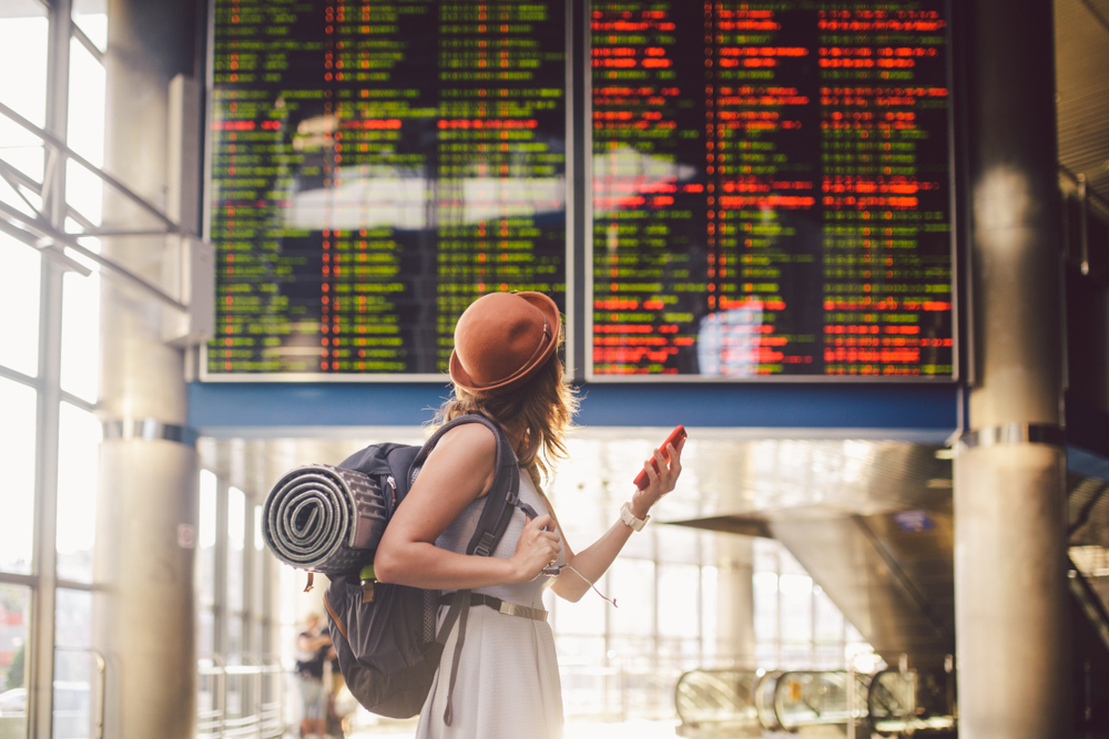 A woman at the airport checking the departures board while carrying her luggage