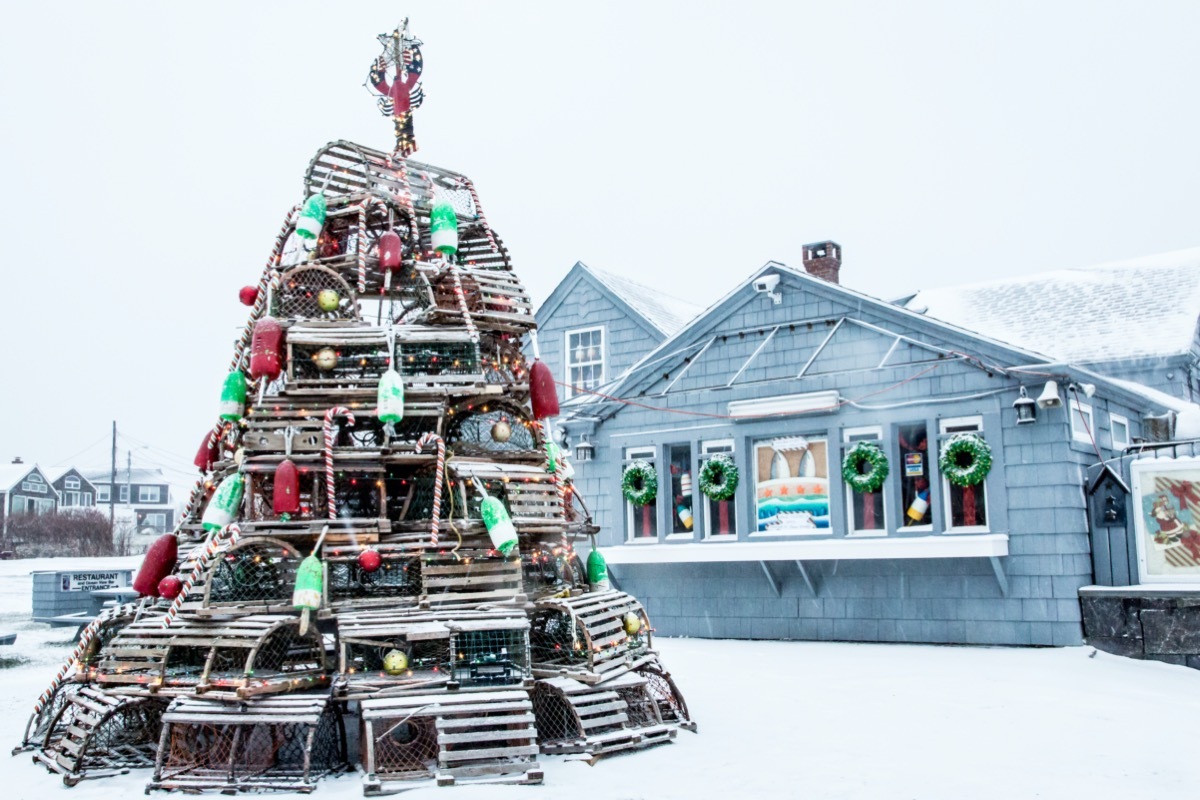 a christmas tree made out of lobster traps and buoys in front of a Maine seafood shack on a snowy day
