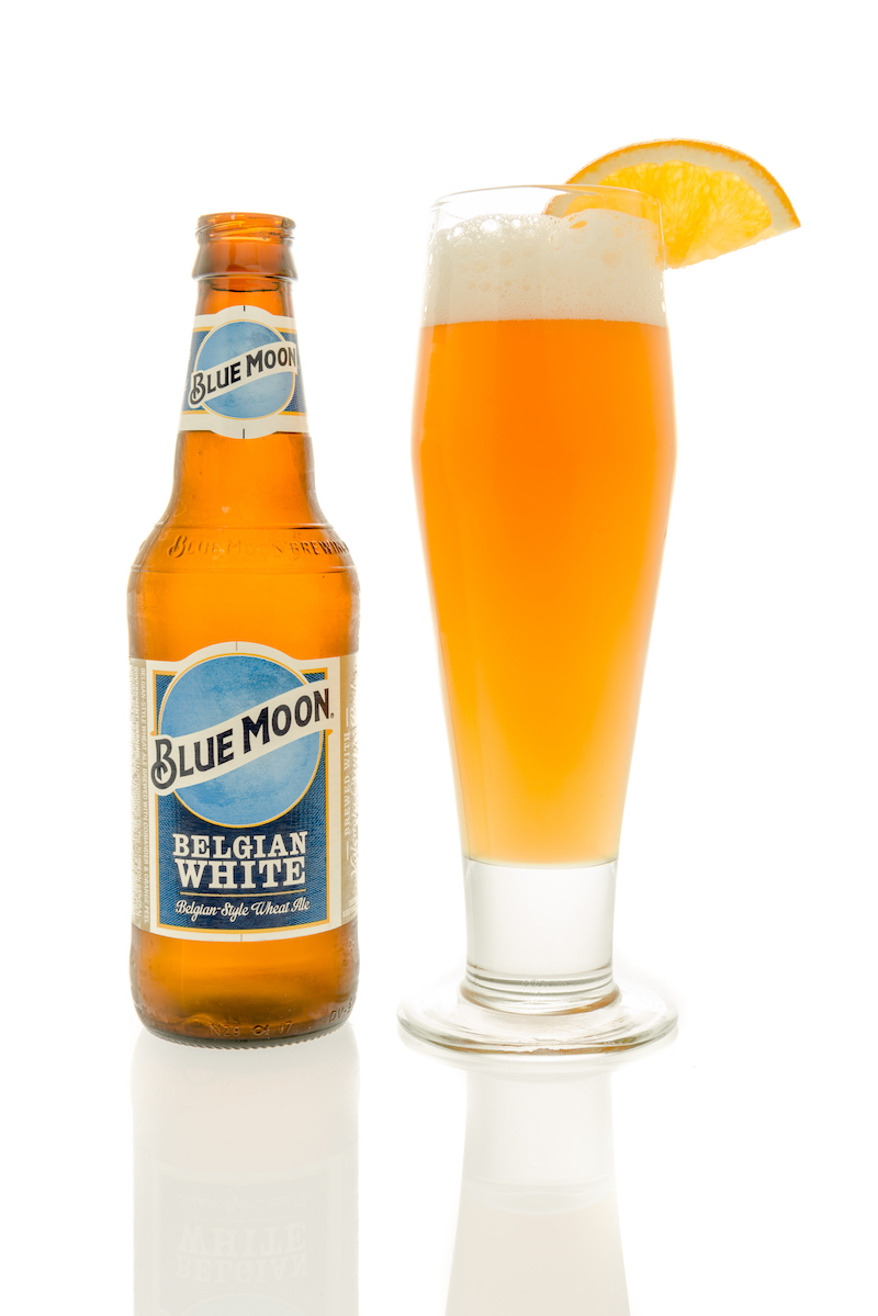 A bottle of Blue Moon beer with a glass and slice of orange on an isolated background.