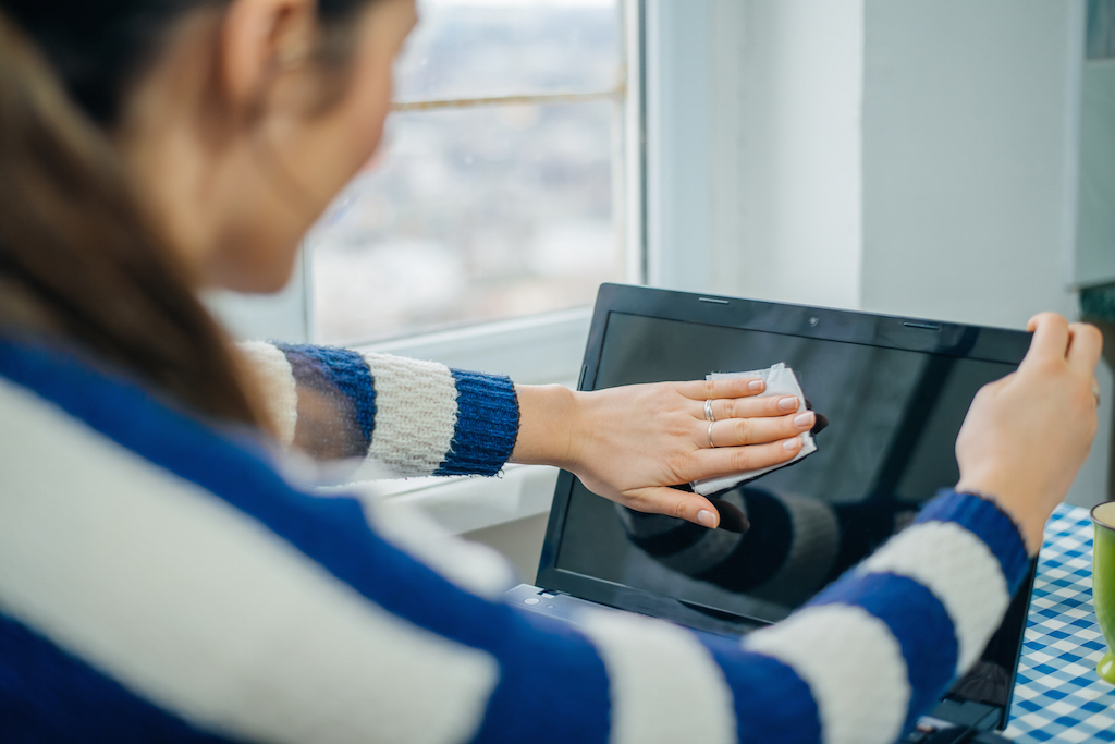 Woman is cleaning her computer screen with a cloth.