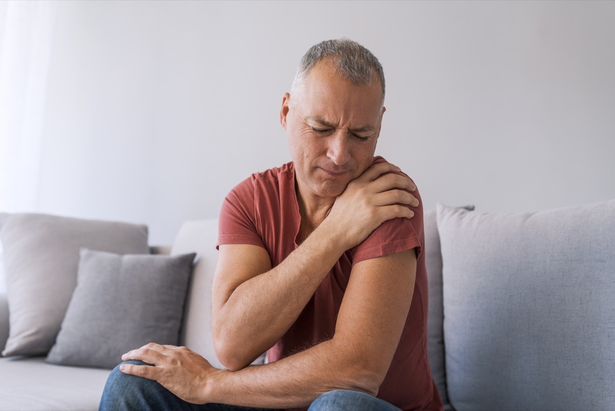 Photo of mature man suffering from pain in shoulder, closeup. People, healthcare and problem concept - unhappy man suffering from neck or shoulder pain at home. Shoulder pain Caused by not taking care of health.
