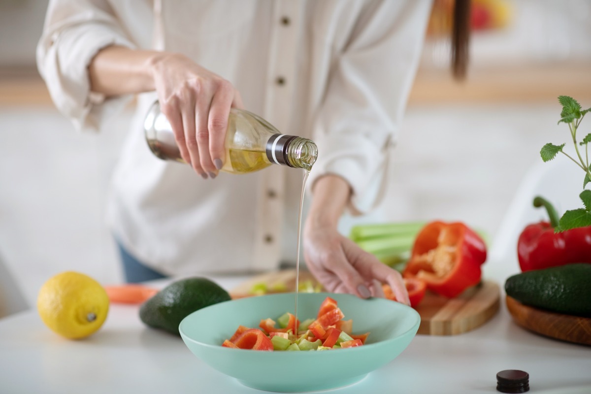 Woman pouring olive oil on salad with avocado