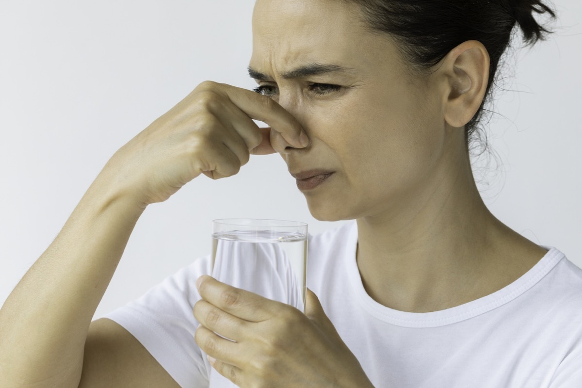 female holding nose and a glass of water in the other hand. Representing bad smell, disgust and water pollution issues.