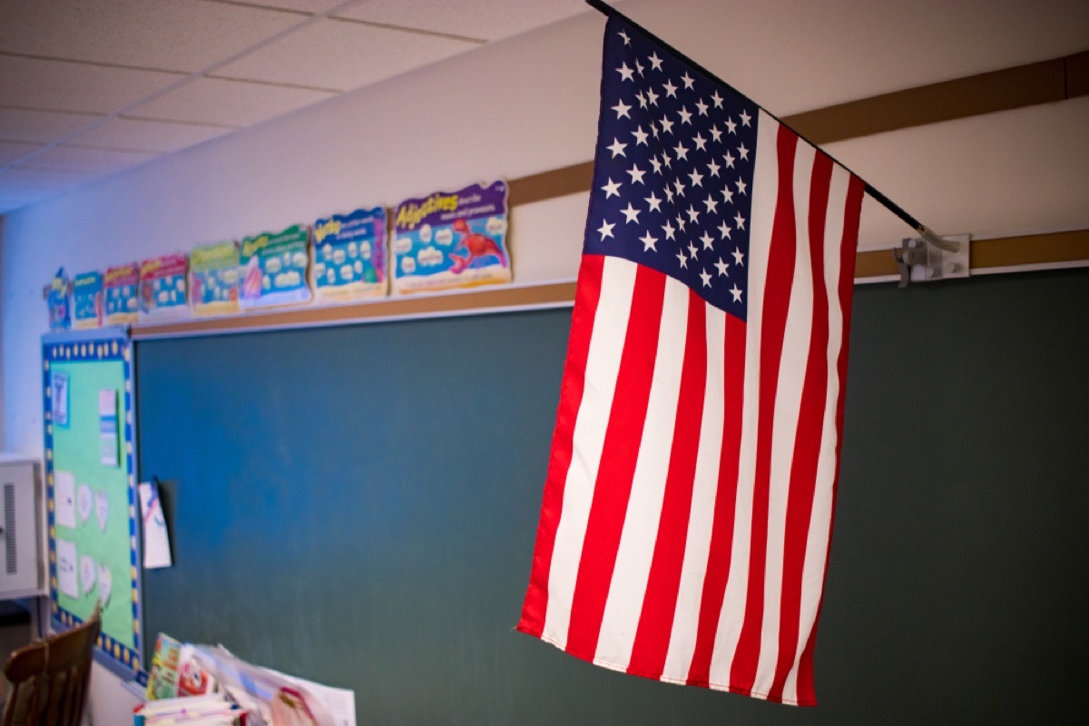 close up of an american flag hanging above a chalkboard in a classroom