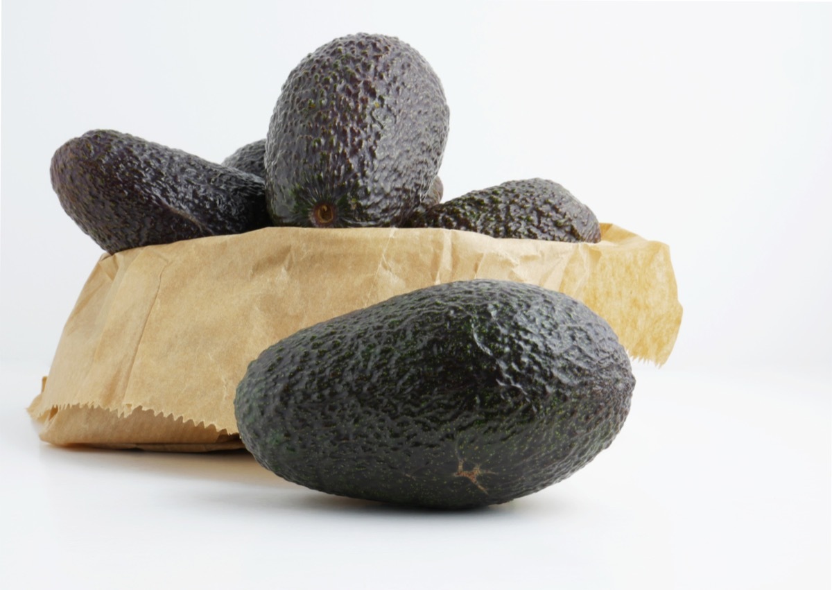 Tropical fruit, avocados on the table next to a kraft paper bag.