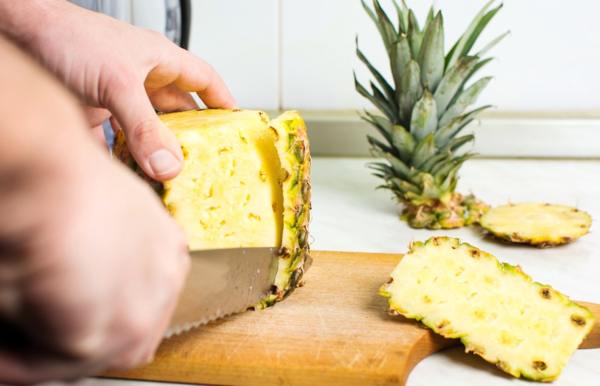 close up of person peeling pineapple with a knife