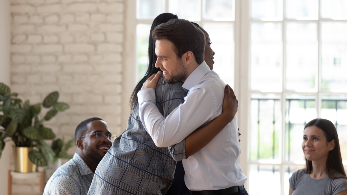 young white man hugging black female coworker
