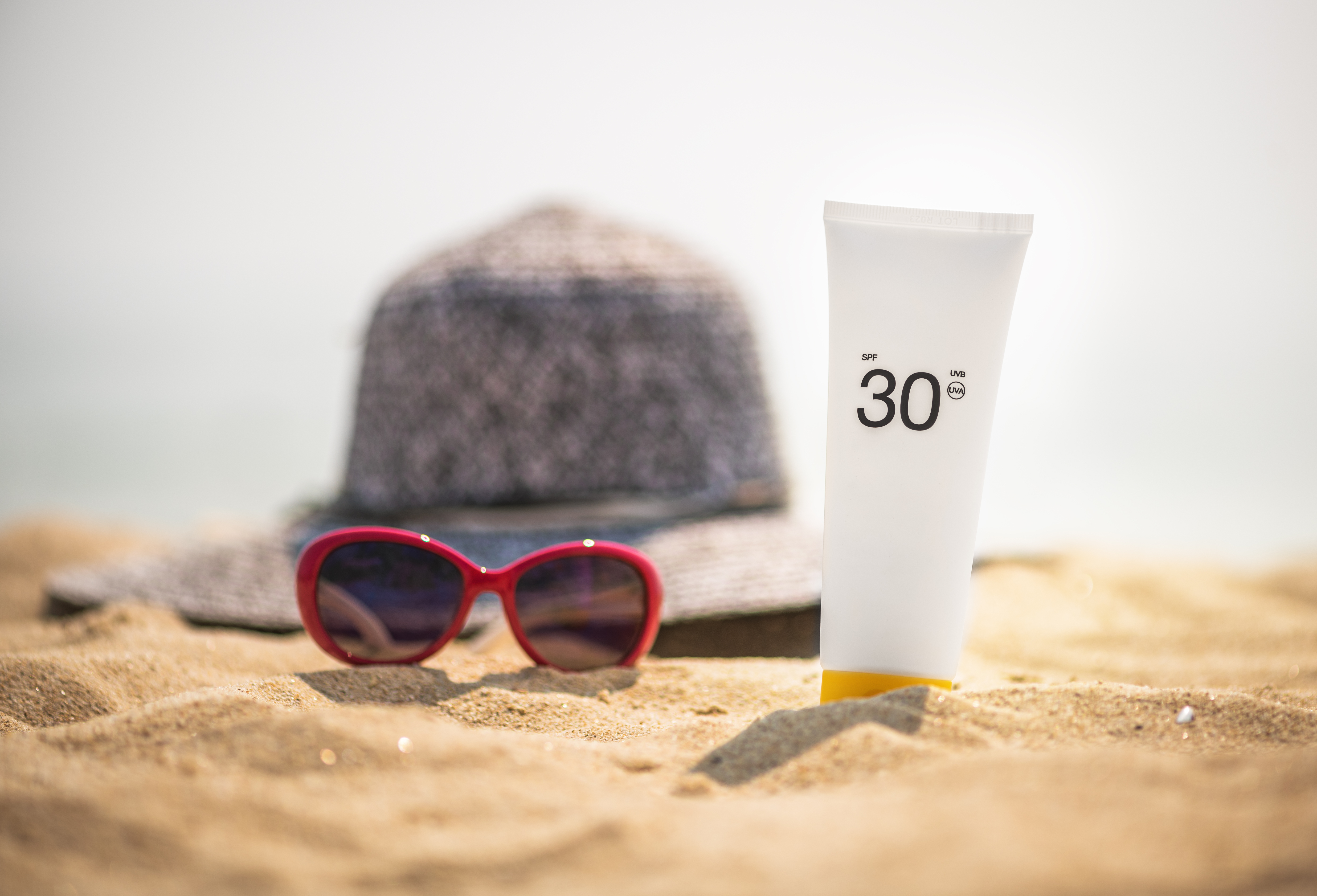 sunglasses and SPF suncreen sitting on a beach, healthy-skin-after-40-spf