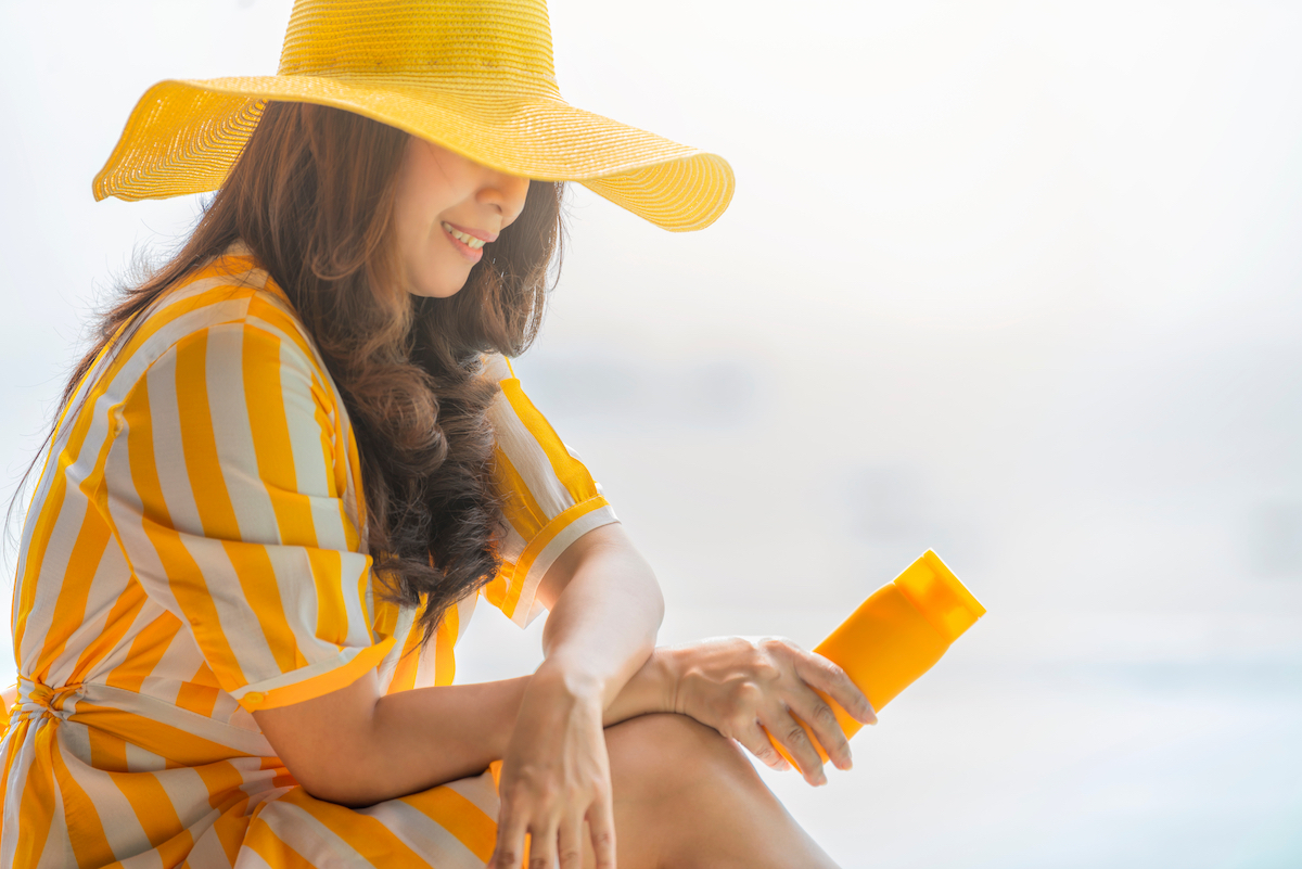 profile of asian woman wearing yellow hat applying sunscreen