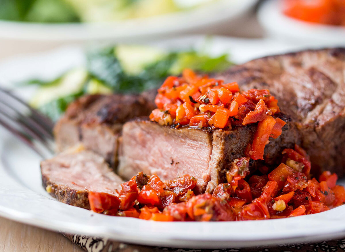 sliced medium well cooked steak dish on white plate with tomato topping