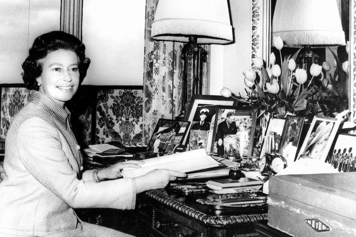 Queen Elizabeth II preparing for her silver jubilee tours, 1977, sitting at desk in front of photos and diary